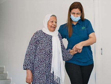 Carer assists elderly woman in a floral dress and scarf with In home support provider